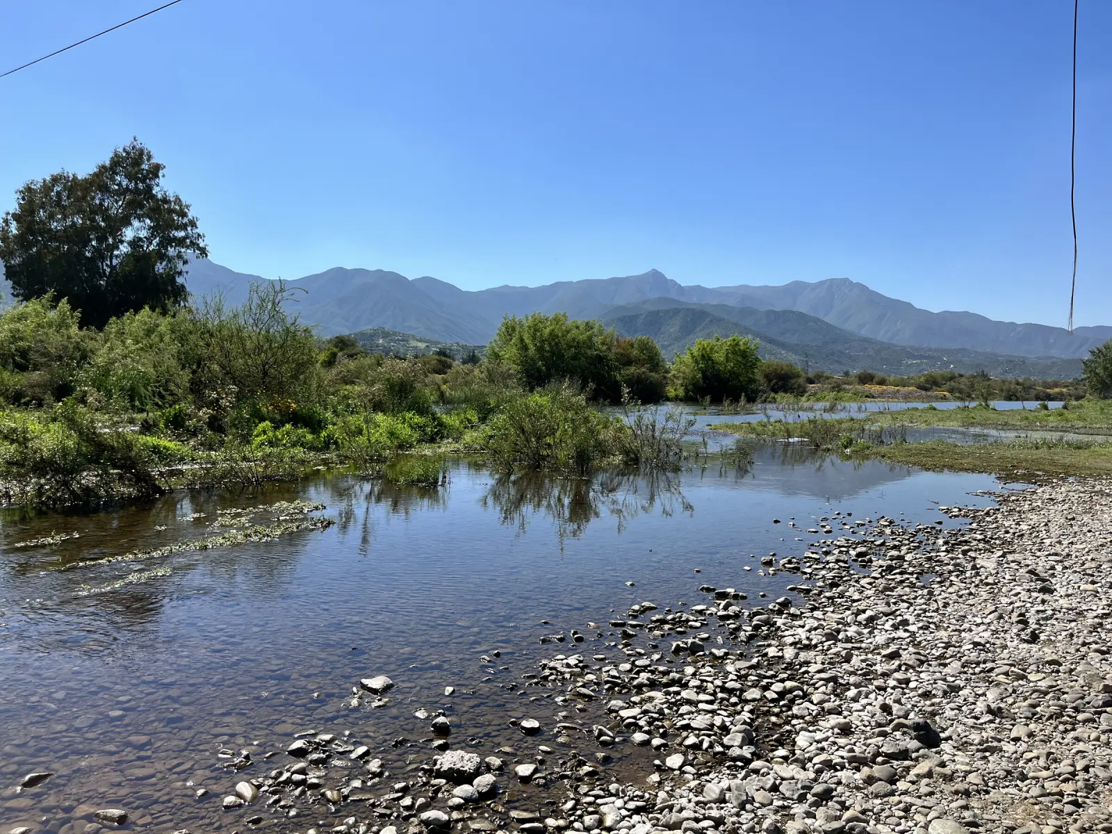 Remanso del río con vegetación en las orillas y la cordillera al fondo, cerca de la Piedra Tacita