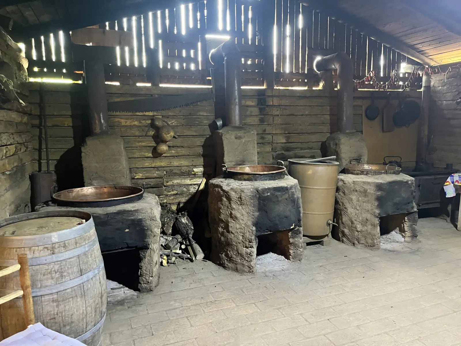 Cocina de Chicha Daine con ollas de cobre sobre fogones de barro y piedra, y un barril