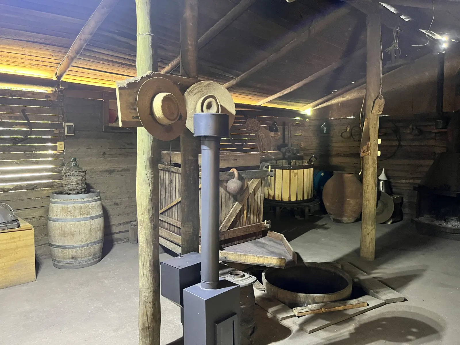 Bodega de Chicha Daine con prensa de madera, barricas, tinajas de greda y sombreros colgados