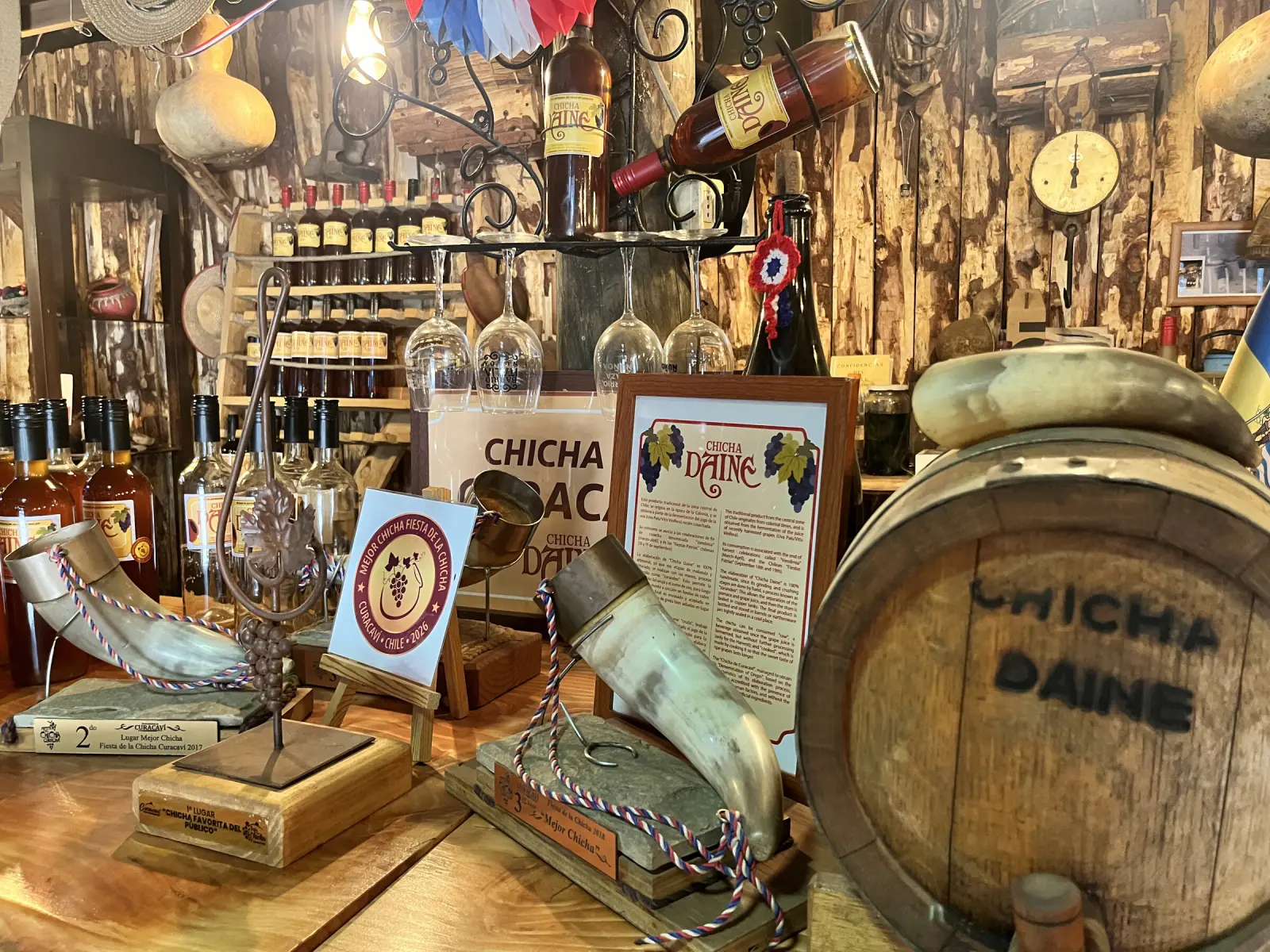 Botellas de chicha, cachos y reconocimientos de la Fiesta de la Chicha sobre el mesón de Chicha Daine